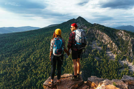 A traveling couple in hiking gear in the mountains at sunset. Two tourists on the top of the mountain. A man and a woman in the mountains. Hiking in the mountains with backpacks. Two travelersの写真素材