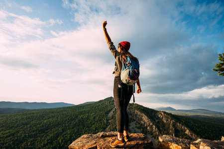 Rear view of a man standing against the background of a mountain with his hand raised. A man in the mountains raises his hand. A man on the background of mountains. A trip to the mountains. Copy spaceの写真素材