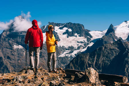 Young couple doing Nordic walking in the mountains, rear view. An active couple is engaged in Hiking. A young couple is engaged in tracking. Trekking and Nordic walking. Hiking. Copy spaceの写真素材