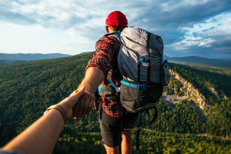 Portrait of a man holding his woman's hand while walking along a mountain range. The couple is enjoying a walk in nature. A girl holds her boyfriend's hand in the mountains. A trip to the mountainsの写真素材
