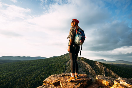 A woman meets the sunset in the mountains. Man travels in the mountains. Mountain tourism. The journey to the mountains. Man on the background of a beautiful evening landscape. Copy spaceの写真素材