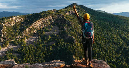 The traveler is happy to climb the mountain, panorama. Man travels in the mountains. Mountain tourism. The journey to the mountains. Man on the background of a beautiful evening landscape. Copy spaceの写真素材