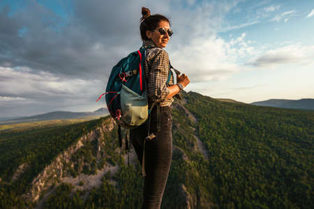 Portrait of a female traveler in the mountains. Adventure, travel and hiking concept. A happy woman enjoys the sunlight during a hike in the mountains. The traveler looks at the camera. Copy spaceの写真素材