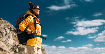 Tourist with a backpack against the sky, panorama. Portrait of a traveler in yellow clothes against the sky. Portrait of a woman in tourist gear traveling with a backpack. Copy spaceの写真素材