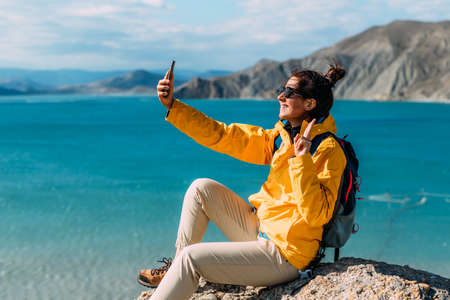 A traveler takes a selfie on her phone against the background of the sea, Close-up. A traveler on the seashore. A girl holds a phone in her hands against the background of a beautiful sea.の写真素材