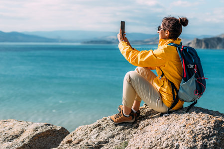 A traveler takes a selfie on her phone against the background of the sea, Close-up. Travel and active lifestyle concept. A woman holds a phone in her hands against the background of the blue sea.の写真素材