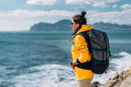 A woman with a backpack on the background of the sea. Portrait of a woman in tourist gear on the background of the sea. The concept of travel and an active lifestyle. A tourist girl on the seashore.の写真素材