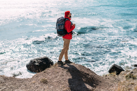 A man with a backpack on the background of the sea. Portrait of a man in tourist gear on the background of the sea. The concept of travel and an active lifestyle. A male tourist on the seashore.の写真素材