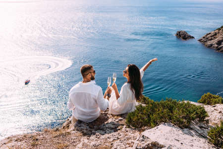 A couple in love celebrates their engagement on the seashore. A beautiful couple drinks champagne by the sea. Honeymoon trip. Lovers on the beach. Wedding travel. Couple on vacation. Copy spaceの写真素材