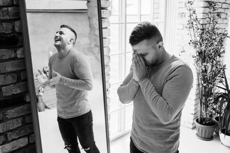A man with bipolar disorder at the mirror. Bipolar affective disorder. A person with manic-depressive psychosis. Mental illness. A person with depression. A man is reflected in the mirrorの写真素材