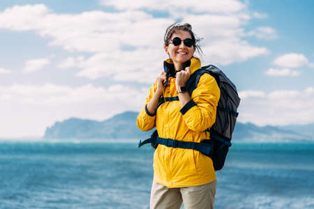 Portrait of a happy traveler tourist on the background of the sea. Portrait of a young woman in tourist gear. Portrait of a beautiful female traveler on the background of the sea. Smiling touristの写真素材