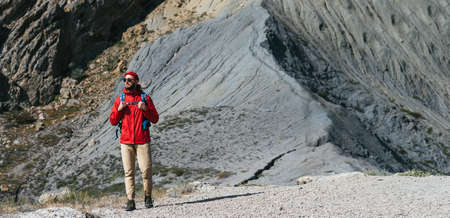 A male tourist with a backpack descends from the mountains, panorama. A traveler on the background of mountains. A tourist with a backpack on the background of mountains. Copy spaceの写真素材