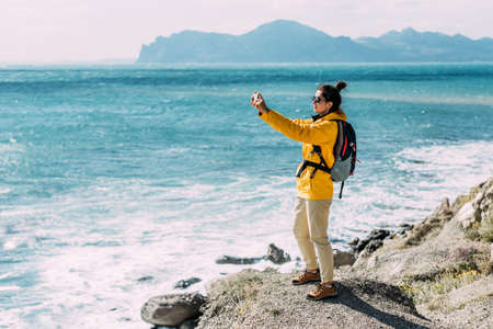 A traveler with a phone on the background of the sea. A travel blogger takes a photo video on his phone against the background of the sea. Travel and active lifestyle concept. Tourist by the seaの写真素材
