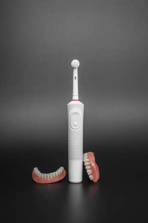 Dental care with an electric brush. Dentures and an electric brush on a black background. Acrylic dentures. Oral hygiene. Orthopedic dentistry. False teeth. Teeth and toothbrush on a dark backgroundの写真素材