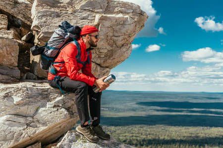 A male tourist is resting after a hard climb up the mountain. A traveler among the Rocky Mountains. A man is a traveler with a backpack among the rocks. Backpacking in the mountains. Copy spaceの写真素材
