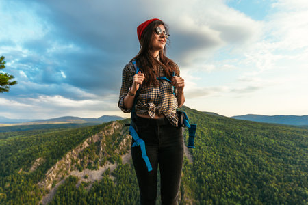 Portrait of a female traveler in the mountains. Adventure, travel and hiking concept. A happy woman enjoys the sunlight during a hike in the mountains. Portrait of a traveler in a red hat. Copy spaceの写真素材