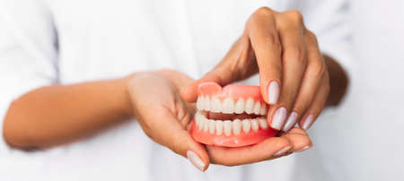 Dental prosthesis in the hands of the doctor close-up. Dentist holding ceramic dental bridge. Front view of complete denture. Dentistry conceptual photo. Prosthetic dentistry. False teethの写真素材