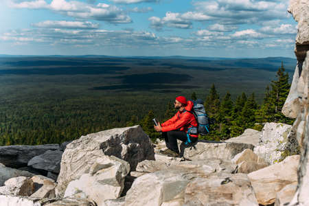 A male tourist is resting after a hard climb up the mountain. A traveler among the Rocky Mountains. A man is a traveler with a backpack among the rocks. Backpacking in the mountains. Copy spaceの写真素材