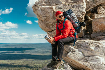 A male tourist is resting after a hard climb up the mountain. A traveler among the Rocky Mountains. A man is a traveler with a backpack among the rocks. Backpacking in the mountains. Copy spaceの写真素材