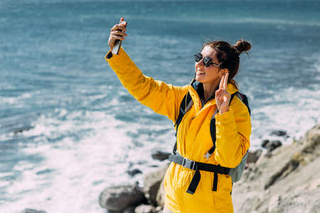 A tourist girl is talking on a video call against the background of the sea. A traveler takes a selfie on her smartphone against the background of the sea. A traveler on the seashore. Copy spaceの写真素材