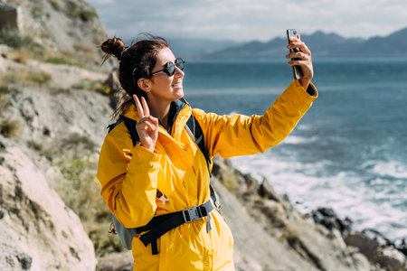 A traveler takes a selfie on her phone against the background of the sea, Close-up. Travel and active lifestyle concept. A woman holds a phone in her hands against the background of the blue seaの写真素材