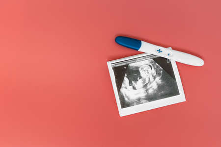 A positive pregnancy test and ultrasound photo on a pink background. A positive pregnancy test...