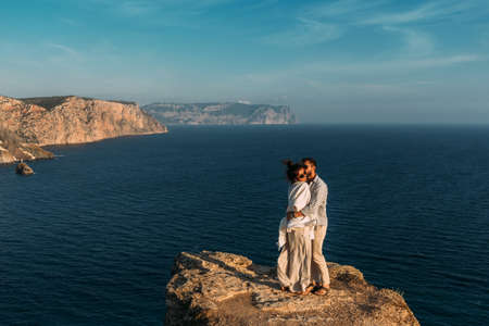 Couple in love at dawn by the sea. Honeymoon. Honeymoon trip. Boy and girl at the sea. Man and woman traveling. Couple hugs. Couple kissing. Newly married couple. Wedding travel. Holiday romanceの写真素材