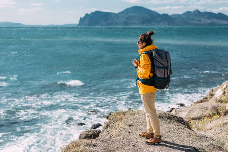A traveler with a backpack on the background of the sea, rear view. Female traveler on the background of the blue sea, panorama. A lonely traveler on the seashore. Tourist banner. Copy spaceの写真素材