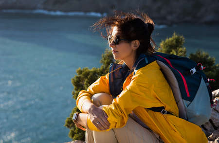 A woman with a backpack on the background of the sea. Portrait of a woman in tourist gear on the background of the sea. The concept of travel and an active lifestyle. A tourist girl on the seashore.の写真素材