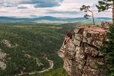 A male traveler is sitting on a rock with a bird's-eye view of the forest. The concept of recreation...