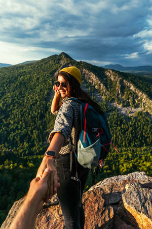 Portrait of a woman holding her man's hand while walking along a mountain range, vertical photo. The couple is enjoying a walk in nature. A guy holds his girlfriend's hand in the mountains. follow meの写真素材
