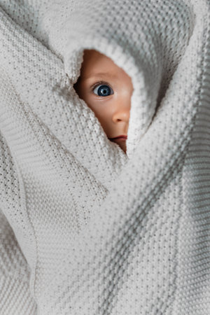 Portrait of a small child covered with a blanket. A beautiful original portrait of a child. The child is under the blanket. A small child peeks out from under the blanketの写真素材