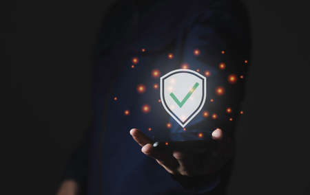 A hand holding smartphone with security icon, protech and check mark computer graphic ligt, modern technology data protech solution conceptの写真素材
