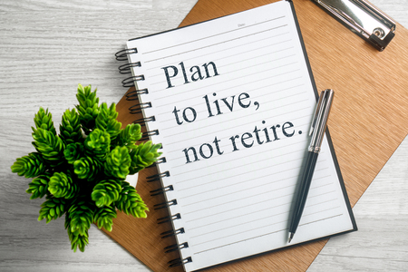 Plan to live not retire. Inspirational quote on notebook with pen, clipboard and potted plant.の写真素材