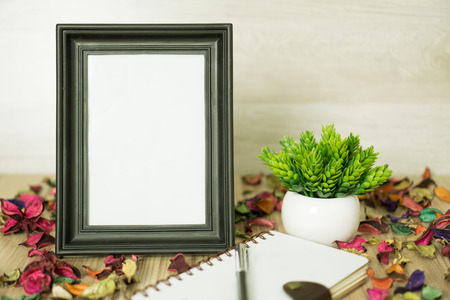 Standing photo frame on wood background with notebook diary, pen, potted plant and dry flower petals. Rustic nostalgia.の写真素材
