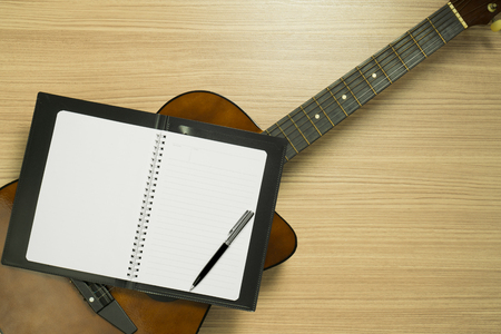 Notebook on top of an acoustic guitar on wood background. Still life flat lay.の写真素材