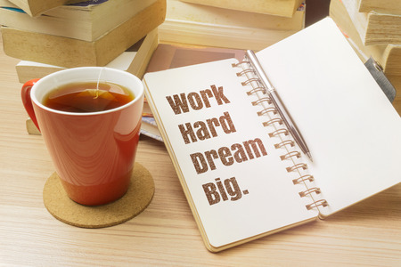 Work hard dream big. Inspirational quote on notebook with pen, cup of tea and pile of books.の写真素材