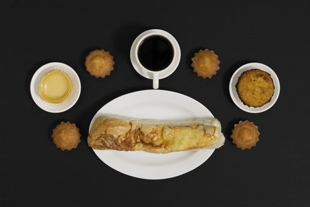Coffee, cakes and bun on black background. Breakfast meal flat lay.の写真素材