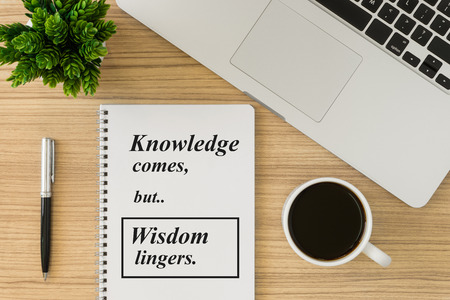Notebook with motivational and inspirational wisdom quote on wood desk. Knowledge comes but wisdom...