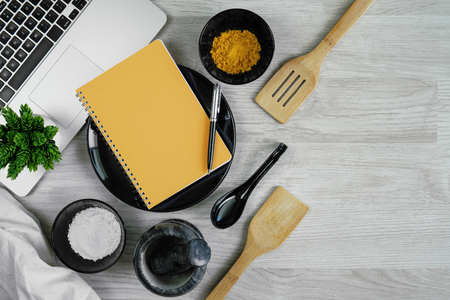 Cutlery set with spices, chilies, mortar, laptop and notebook on wood table background. Kitchen utensils.の写真素材