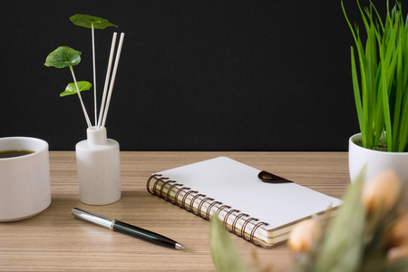 Spiral notebook with coffee cup and potted plant on wood desk with black background.の写真素材