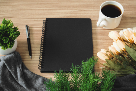Black notebook with coffee cup and flower on wood desk. Text copy space.の写真素材