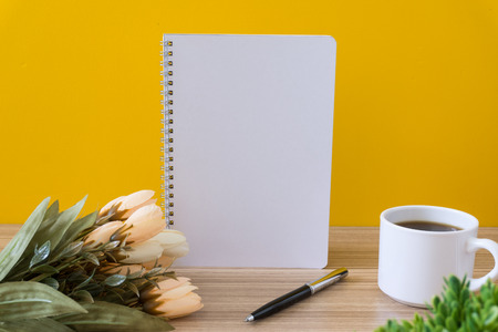 Notebook with coffee cup and flower on wood desk with yellow background. Text copy space.の写真素材