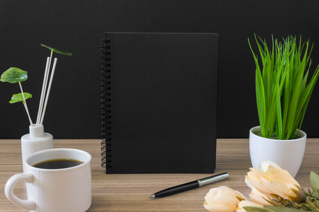 Black notebook with coffee cup and potted plant on wood desk with black background. Text copy space.の写真素材