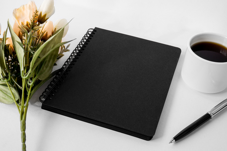 Black notebook with coffee cup and flower on white background. Text copy space.の写真素材