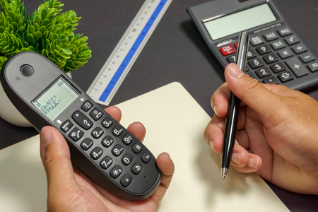 Hands holding phone and pen on office working table.の写真素材