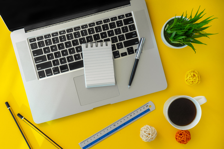 Laptop and small notebook on yellow working desk. Elegant workspace flat lay.の写真素材