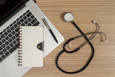 Stethoscope with notebook and laptop on wood background. Medical practitioner working space.の写真素材