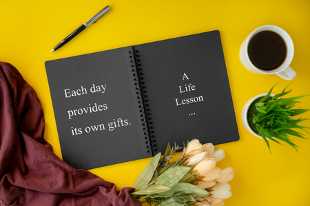 Notebook with wisdom quote and coffee cup on yellow background.の写真素材