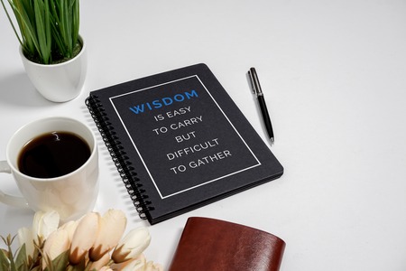 Notebook with wisdom quote and coffee cup on white background.の写真素材